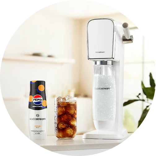 Biały saturator SodaStream z syropem Pepsi Mango Zero Cukru i szklanką z lodem stoją na blacie kuchennym.